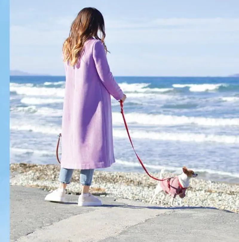 Woman in pink coat walking small dog on leash at beach
