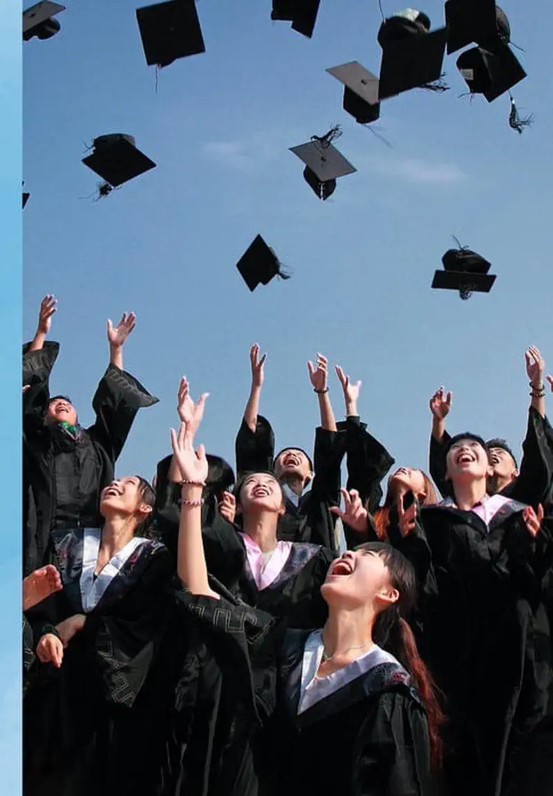 Graduates in black robes joyfully throwing their square black graduation caps into the air against a blue sky.
