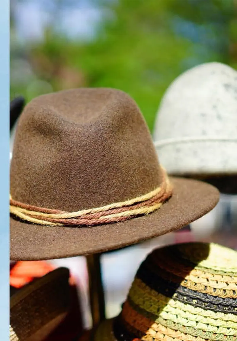A brown felt fedora hat with a braided band displayed alongside other colorful straw and woven hats for sale.