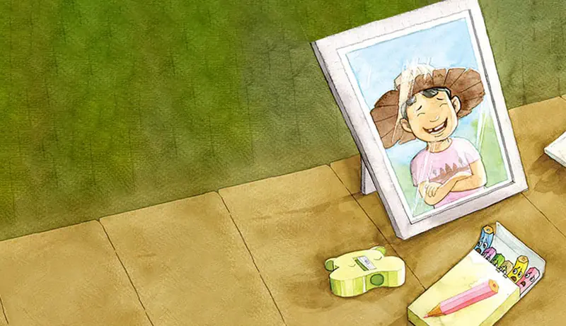 Framed photo of a happy boy wearing a paper hat sits on wooden floor next to pencil sharpener and pencil box.
