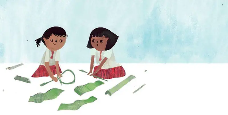 Two girls in school uniforms sit on the ground working with green leaves and stems to make something.