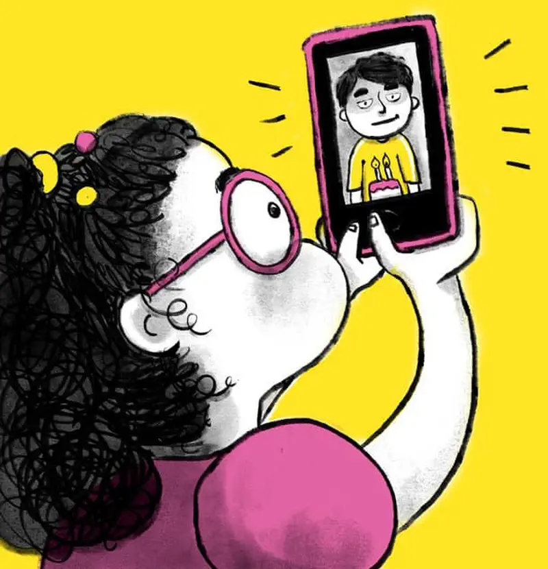 A girl with pink glasses video calls her brother who appears on a tablet screen holding a birthday cake with candles.