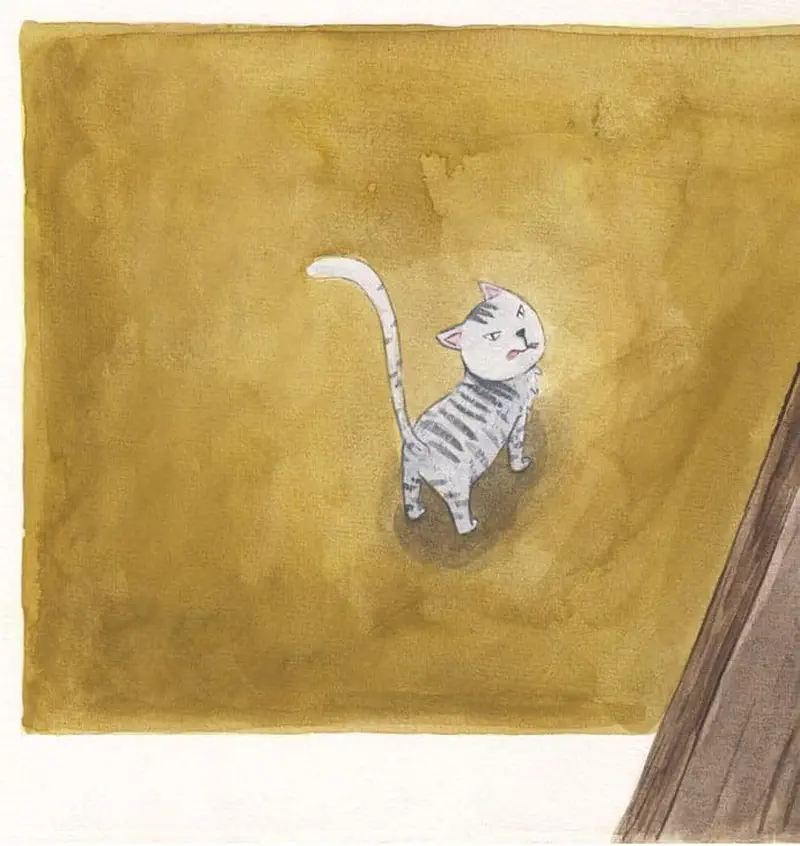 A gray striped cat sits on the floor looking up alertly with its tail raised against a brown background.