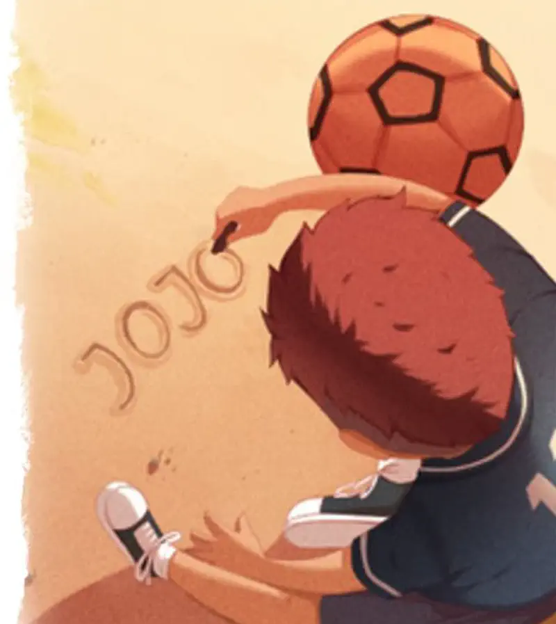 A boy in a blue jersey crouches down writing the name Jojo in the sand with an orange soccer ball beside him.